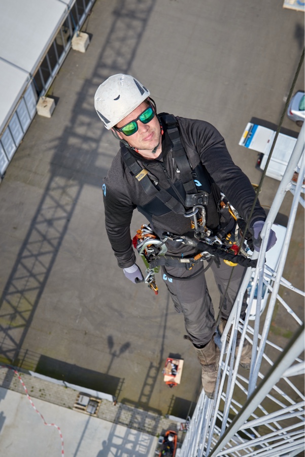 Een man hangt in een harnas in een mast, van bovenaf gefotografeerd